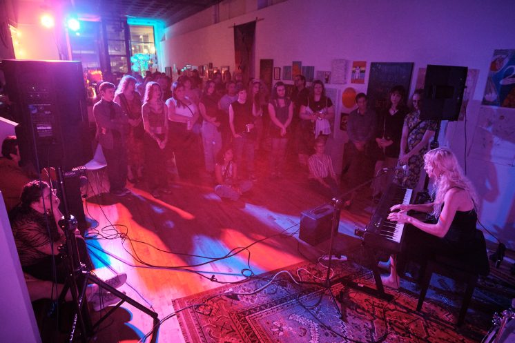 Wide shot of Mara Lovejoy on keys and singing to a crowded room at Prøve Gallery, Sept. 12, 2026